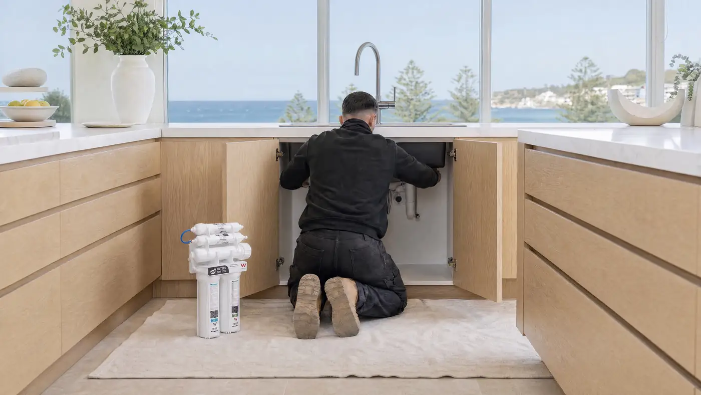 Illustration of Jean-Paul at work under a kitchen sink, seen from behind